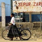 jovem mulher indígena na Guatemala caminha com bicicleta em frente a um edifício degradado
